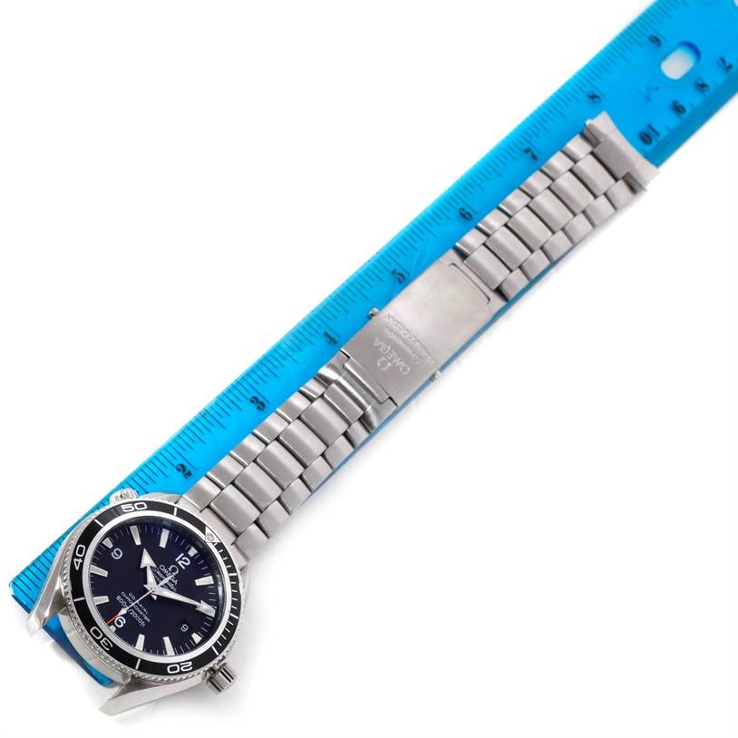 This image shows the Omega Planet Ocean 2201.50.00 Men
s Stainless Steel Black Dial 2201.50.00 Men
s Stainless Steel Black Dial watch laid flat alongside a blue ruler, highlighting the watch face and metallic bracelet.