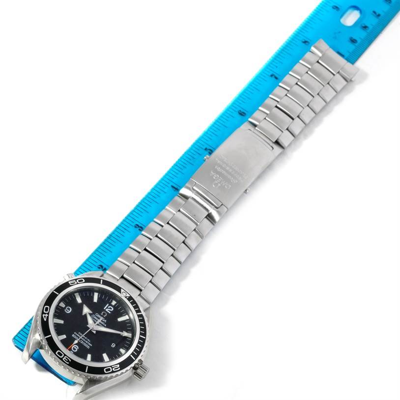 The image shows an Omega Planet Ocean 2200.50.00 Men's Stainless Steel Black Dial 2200.50.00 Men's Stainless Steel Black Dial watch facing up, aligned with a blue ruler to measure its length.