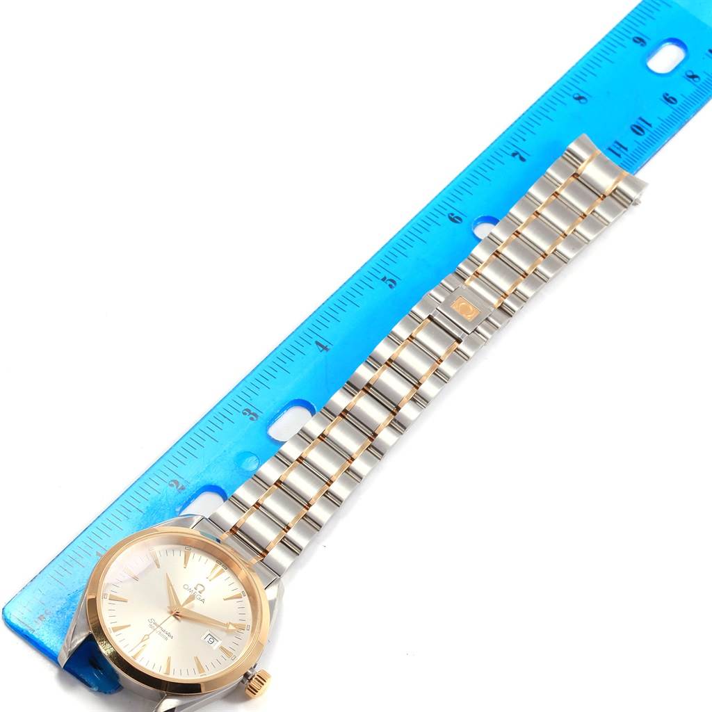 The image shows an Omega Aqua Terra 2317.30.00 Steel and Gold (two tone) Silver Dial 2317.30.00 Steel and Gold (two tone) Silver Dial watch with its face, dial, and metal bracelet laid next to a blue ruler.