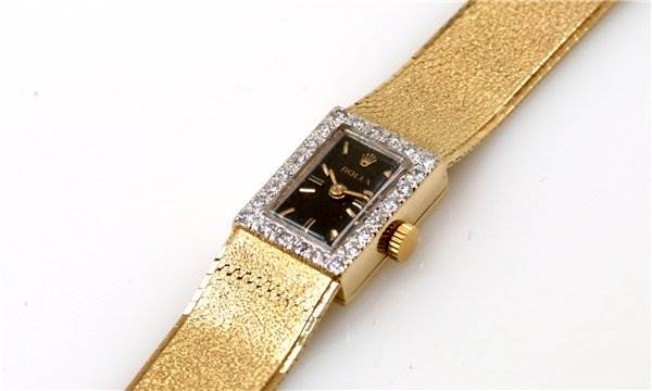 The image shows a Rolex Cocktail Women's Yellow Gold Black Dial Women's Yellow Gold Black Dial model watch with a gold band and a rectangular face adorned with diamonds, viewed from an angled top perspective.