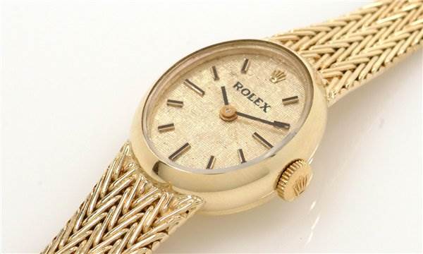 The image shows a close-up, angled view of a Rolex Cocktail 8415 Women's Yellow Gold Champagne Dial 8415 Women's Yellow Gold Champagne Dial model watch, highlighting the dial, crown, and woven bracelet.