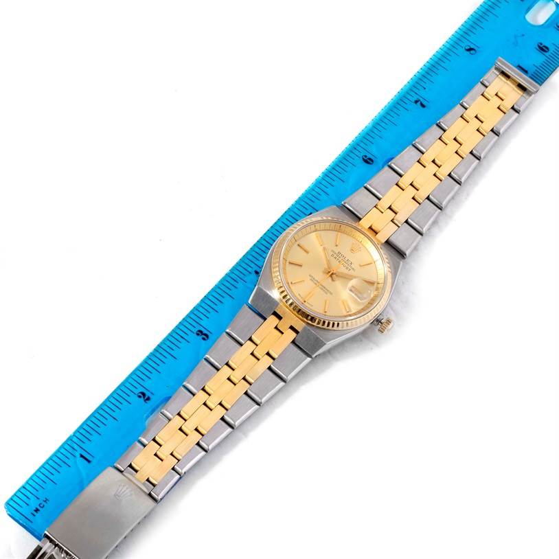 The image shows a Rolex Vintage Collection 1630 Men's Stainless Steel Champagne Dial 1630 Men's Stainless Steel Champagne Dial watch placed flat alongside a blue ruler, highlighting its gold and silver band.