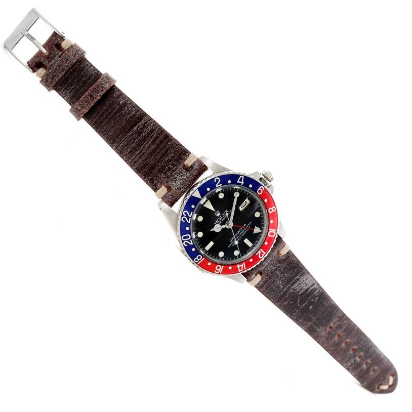 The Vintage Collection Rolex watch is shown from an overhead angle, featuring a brown leather strap and a black dial with a bi-color bezel.