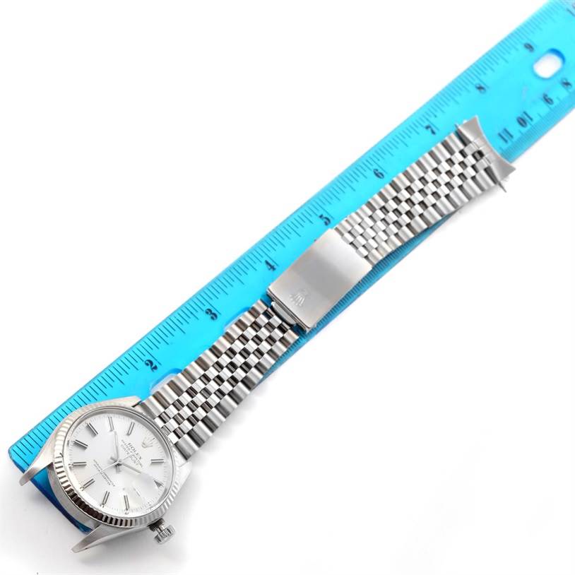 The image shows a top view of a Rolex Vintage Collection 16014 Men's Stainless Steel Silver Dial 16014 Men's Stainless Steel Silver Dial watch and its metal bracelet placed next to a blue ruler.