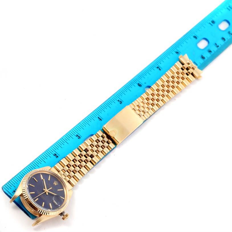 The image shows a side angle view of a Rolex Vintage Collection 15037 Men's Yellow Gold Blue Dial 15037 Men's Yellow Gold Blue Dial watch with a gold band beside a blue ruler.