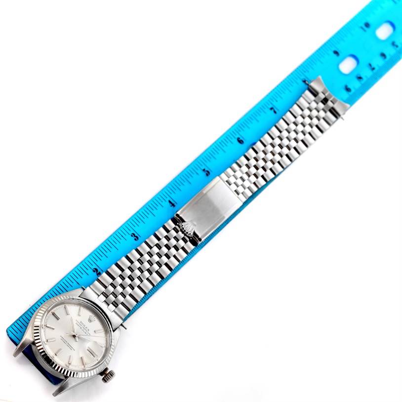 A Rolex Vintage Collection 1601 Men's Stainless Steel Silver Dial 1601 Men's Stainless Steel Silver Dial model watch is shown flat, with its face, bracelet, and clasp visible next to a blue ruler.