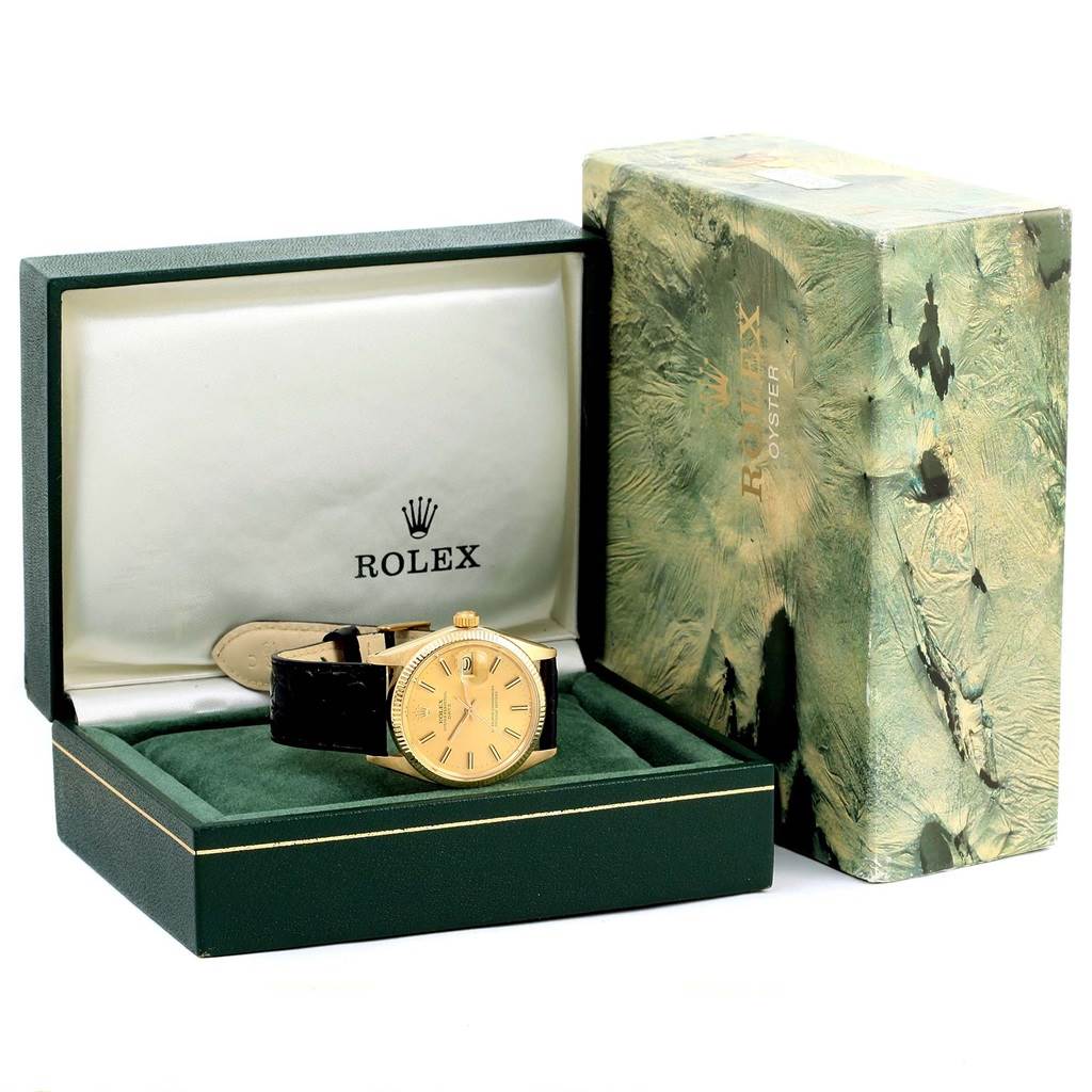 The image displays a Rolex Vintage Collection 1503 Men's Yellow Gold Champagne Dial 1503 Men's Yellow Gold Champagne Dial watch with a gold face and black strap, positioned inside its open box with the outer packaging nearby.