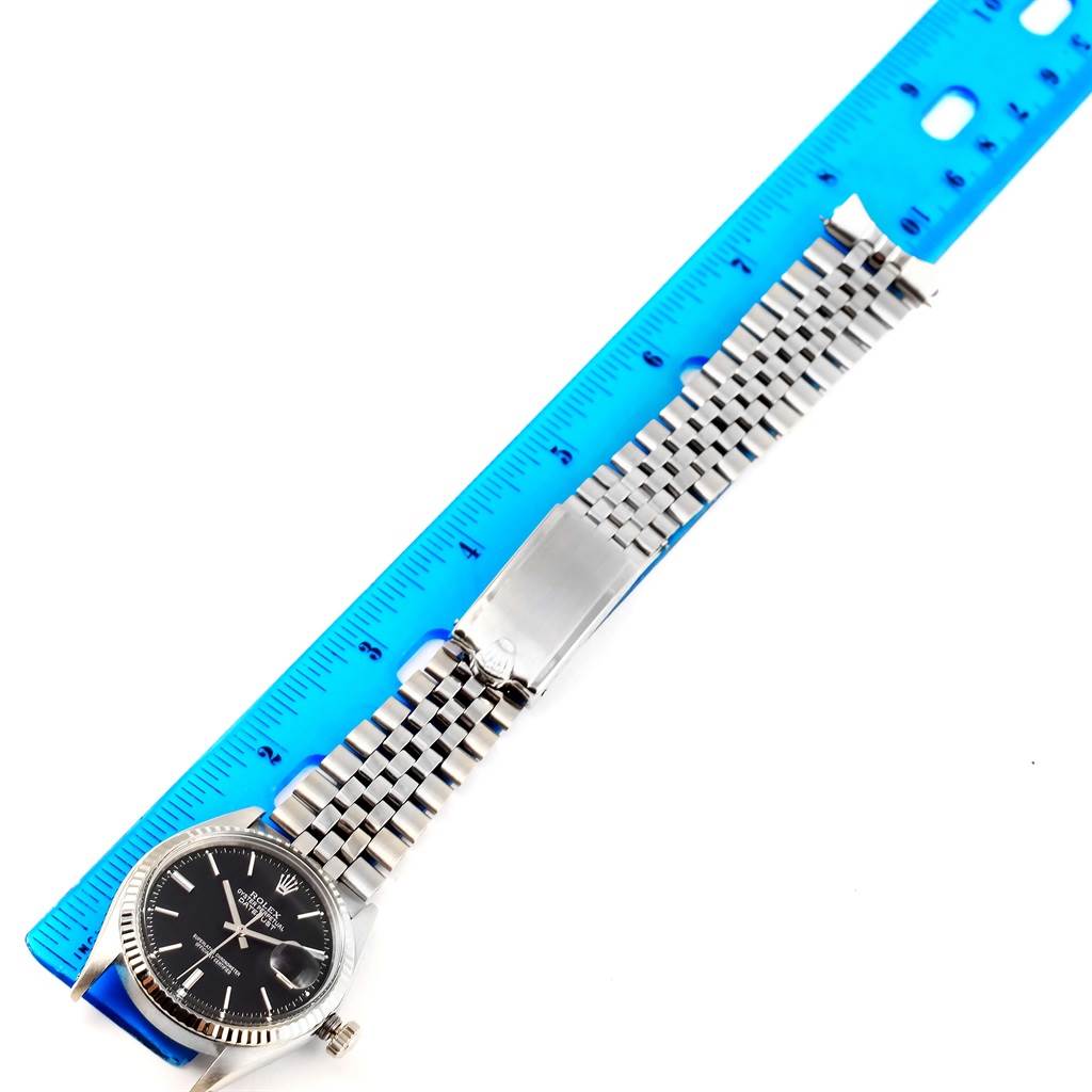 The image shows a Rolex Vintage Collection 1601 Men's Stainless Steel Black Dial 1601 Men's Stainless Steel Black Dial watch flat with its face and bracelet extended next to a blue ruler for size reference.