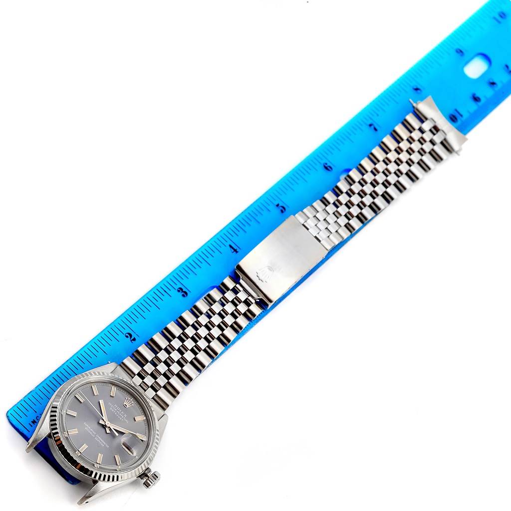 This image shows a top view of a Rolex Vintage Collection 1603 Men's Stainless Steel Grey Dial 1603 Men's Stainless Steel Grey Dial watch with its face, bracelet, and clasp extended beside a blue ruler.