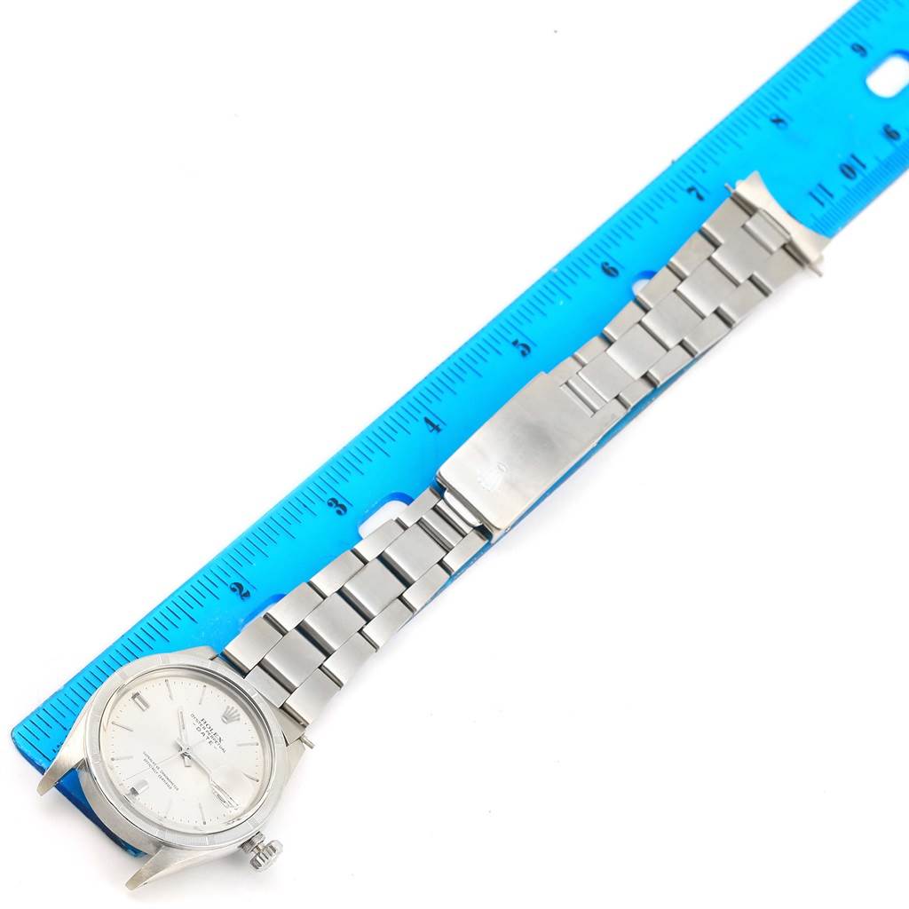 The image shows a Rolex Vintage Collection 1500 Men's Stainless Steel Silver Dial 1500 Men's Stainless Steel Silver Dial model watch laying flat next to a ruler, displaying its face, stainless steel strap, and clasp.