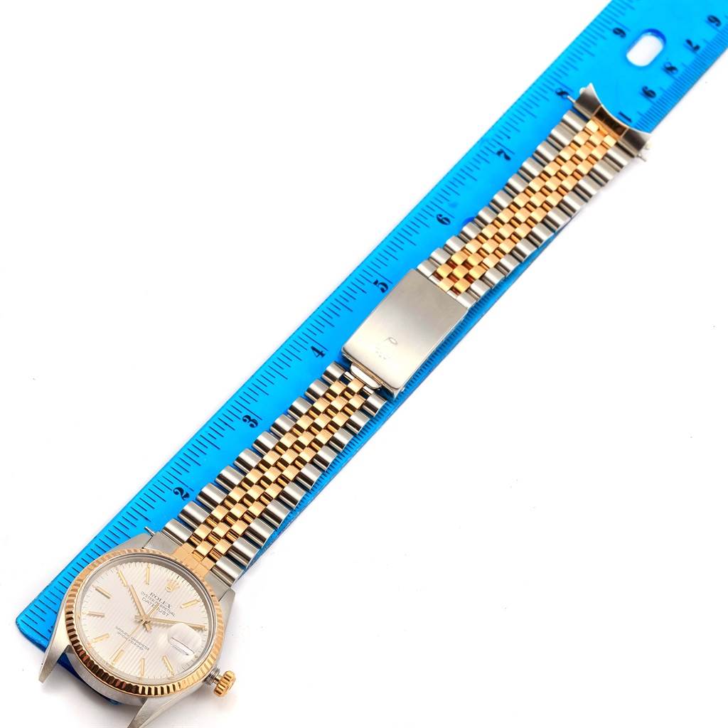 The image shows a Rolex Vintage Collection ROLEX DATEJUST STEEL YELLOW GOLD TAPESTRY DIAL VINTAGE MENS WATCH 16013 Men's Stainless Steel Silver Dial ROLEX DATEJUST STEEL YELLOW GOLD TAPESTRY DIAL VINTAGE MENS WATCH 16013 Men's Stainless Steel Silver Dial watch laid flat next to a blue ruler for size comparison.