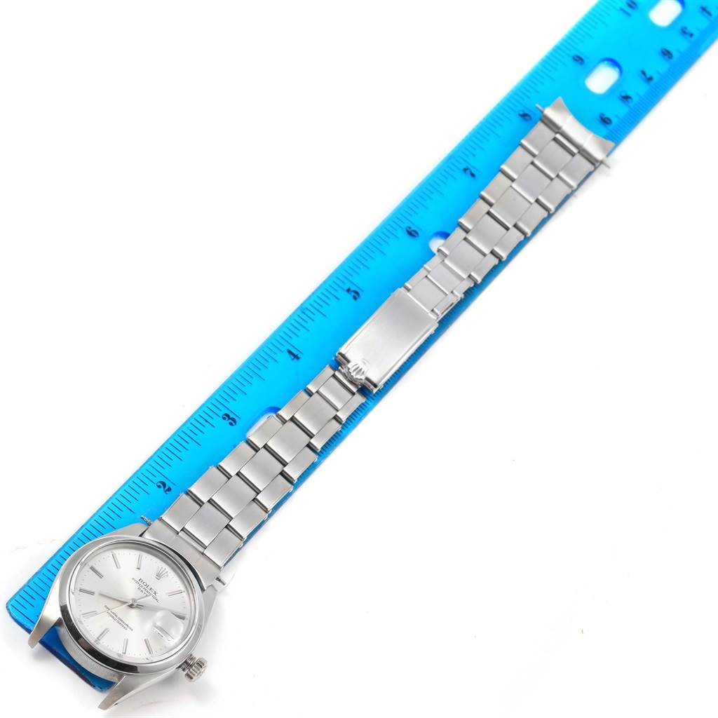 The image shows a Rolex Vintage Collection 1500 Men's Stainless Steel Silver Dial 1500 Men's Stainless Steel Silver Dial watch laid out next to a blue ruler, displaying the watch face, band, and clasp.