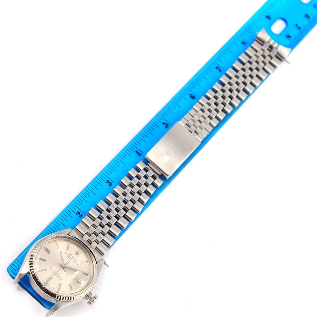 The Rolex Vintage Collection 1601 Men's Stainless Steel Silver Dial 1601 Men's Stainless Steel Silver Dial watch is shown from a top-down angle with its bracelet extended alongside a blue ruler.