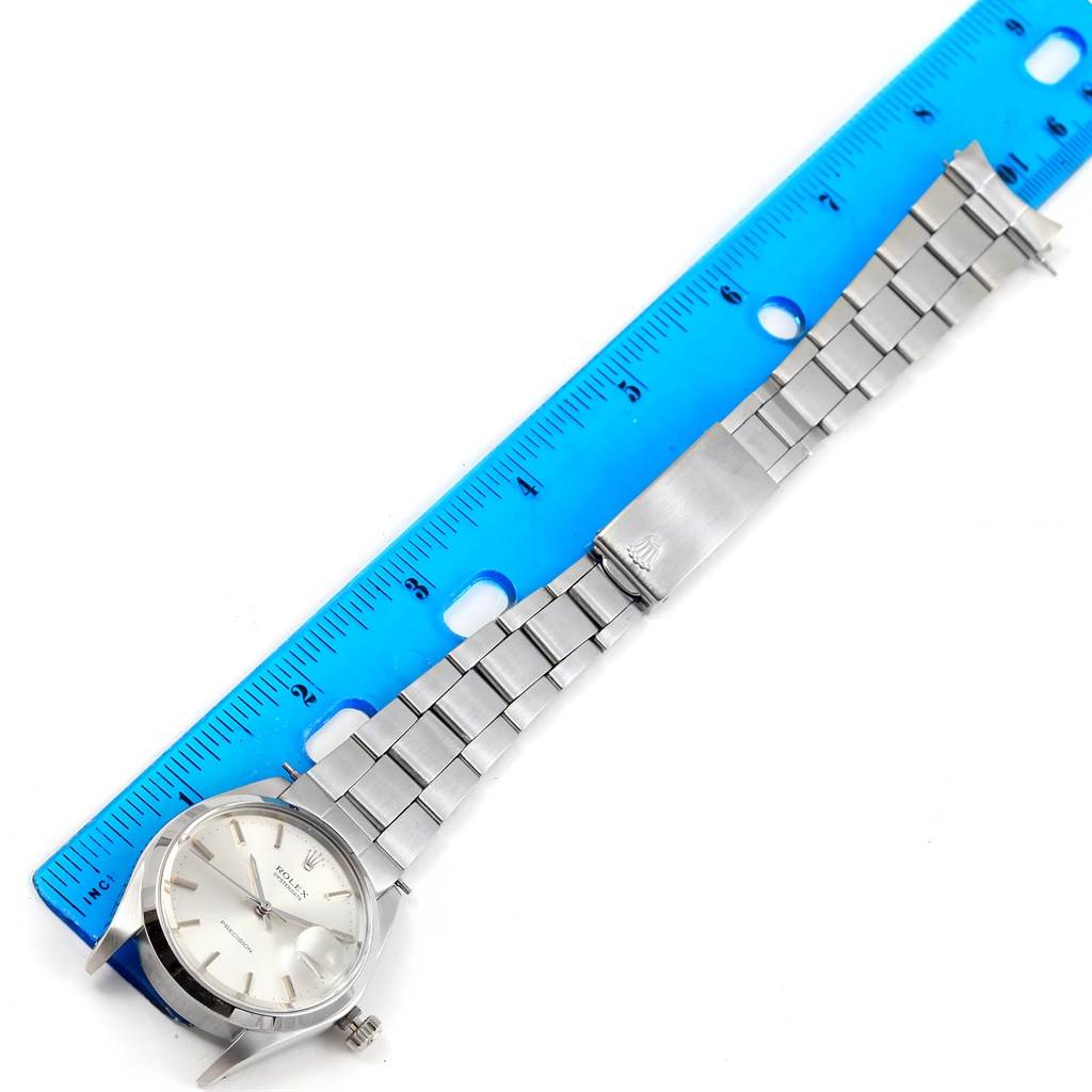 This image shows a Vintage Collection Rolex watch, face up with the stainless steel band and clasp extended next to a blue ruler.