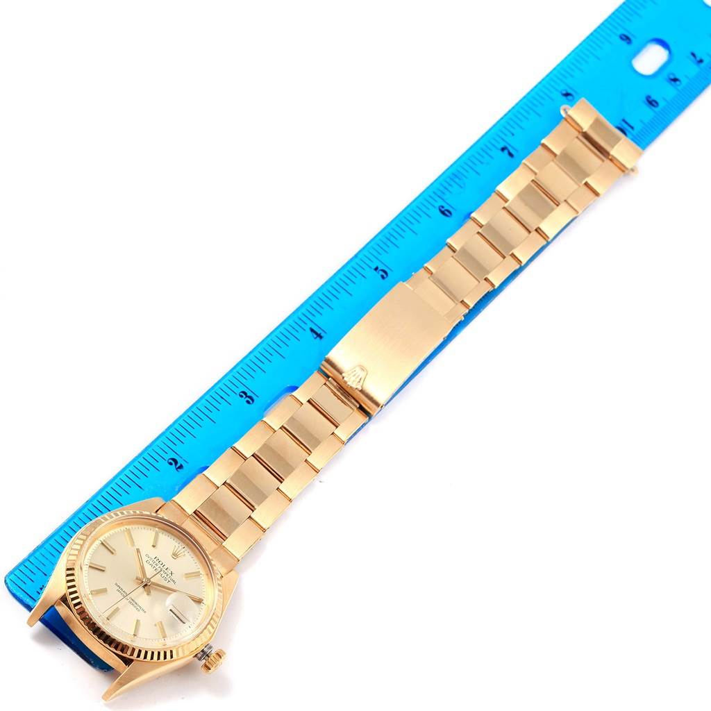 This image shows a Rolex Vintage Collection 1601 Men's Yellow Gold Silver Dial 1601 Men's Yellow Gold Silver Dial watch laying flat with a metal band placed next to a blue ruler for measurement.