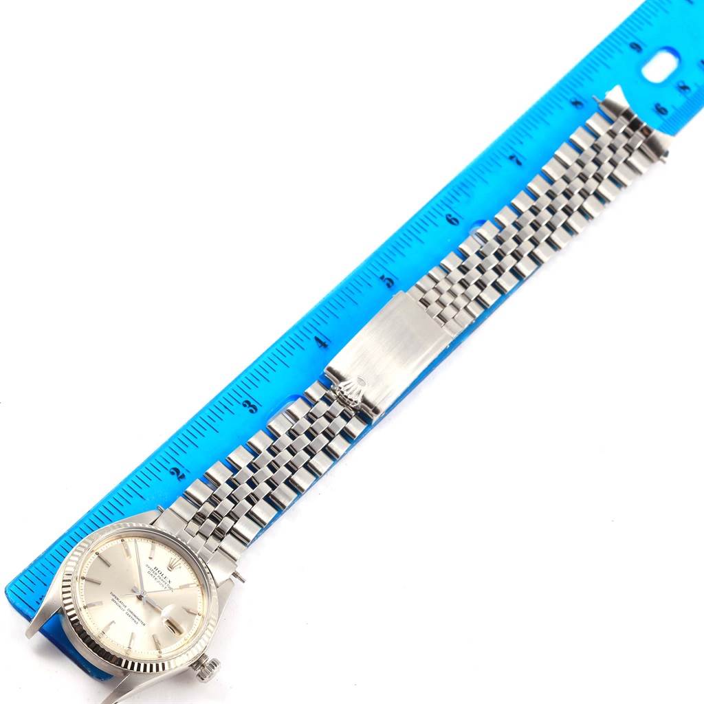 The image shows a Rolex Vintage Collection 1601 Men's Stainless Steel Silver Dial 1601 Men's Stainless Steel Silver Dial model watch laid next to a blue ruler, highlighting the watch case and metal bracelet.