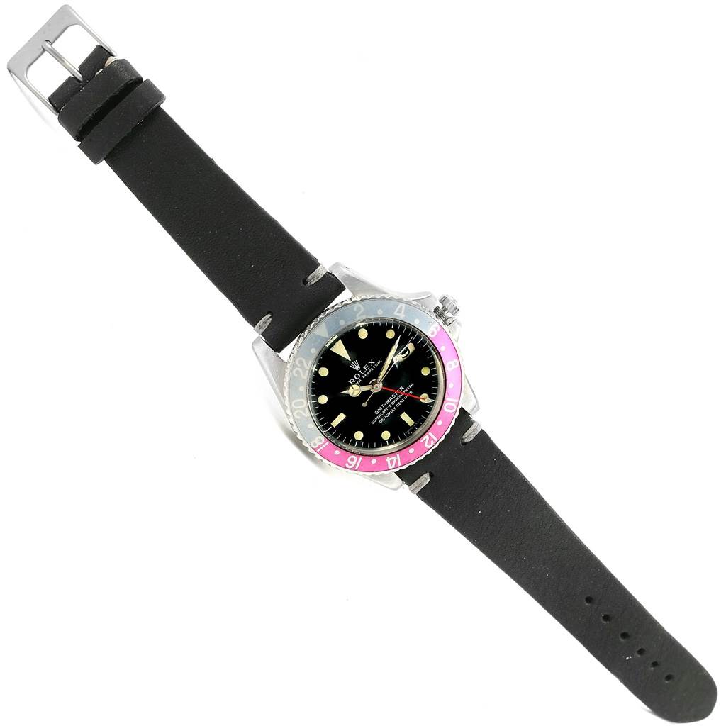 The image shows a top-down view of a Vintage Collection Rolex watch with a black strap and a black and pink bezel.