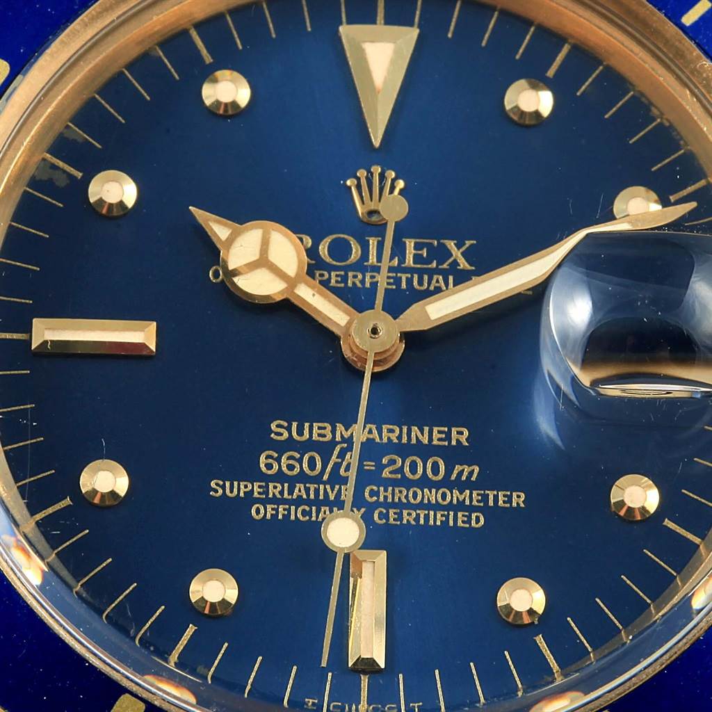 A close-up of a Rolex Submariner Vintage Collection watch's blue dial and gold markers, showing the hands and date magnifier.