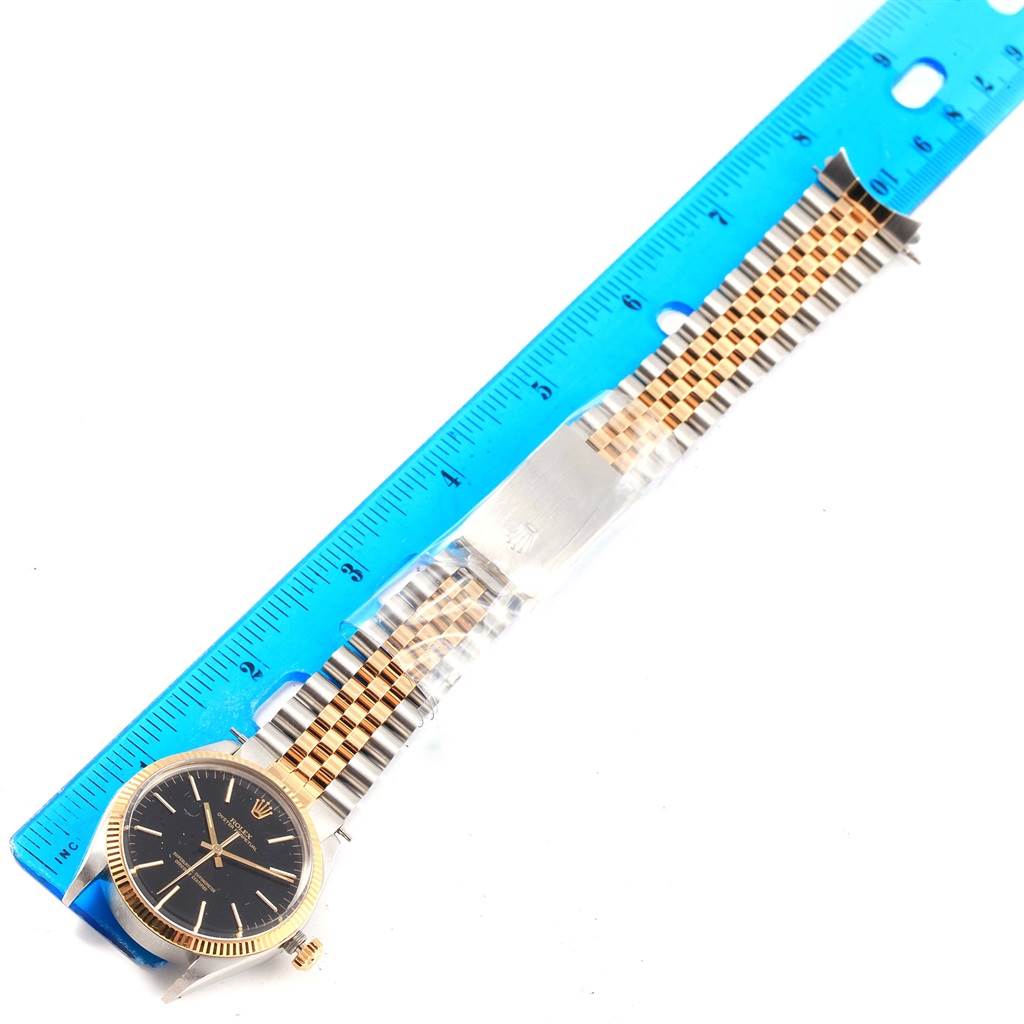 The image shows a side angle of a Rolex Vintage Collection 1005 Men's Steel and Gold (two tone) Black Dial 1005 Men's Steel and Gold (two tone) Black Dial watch with its gold and silver band being measured by a blue ruler.