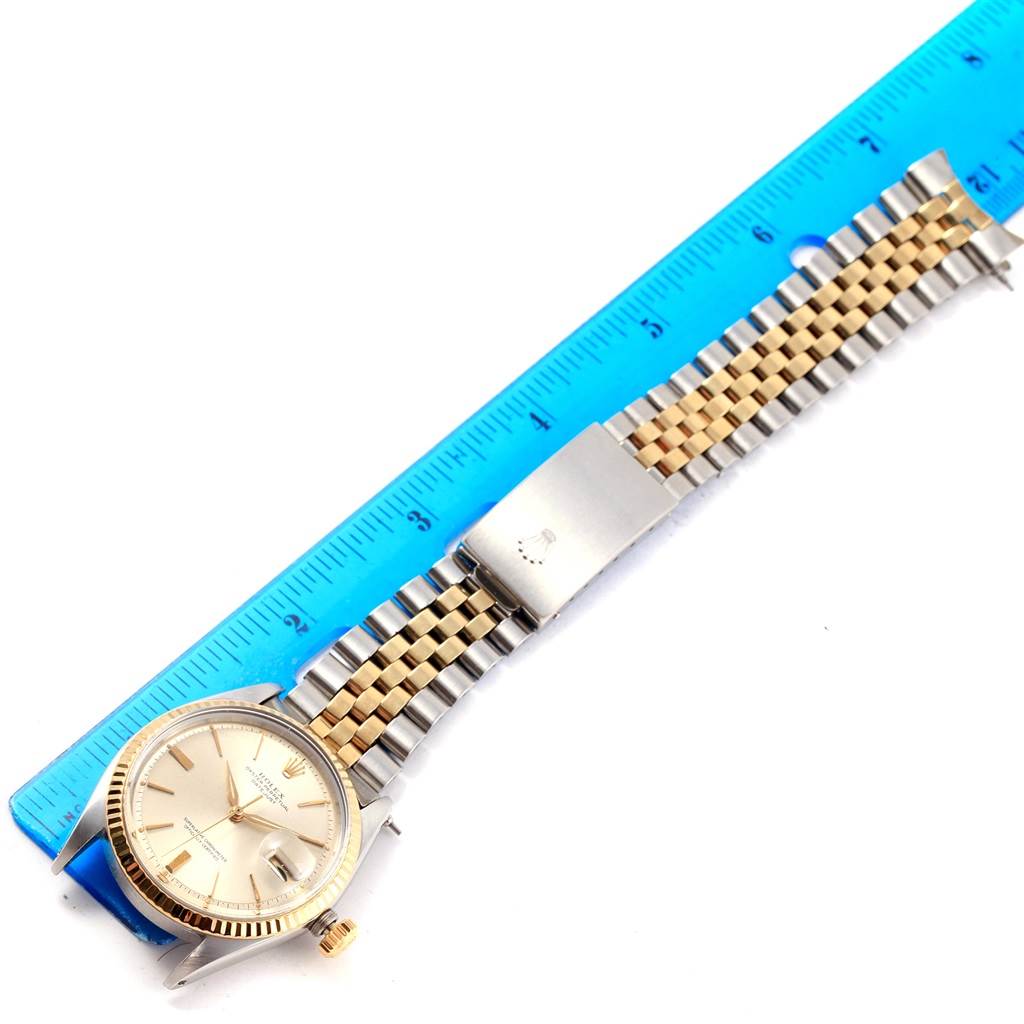 The image shows a Rolex Vintage Collection 1601 Men's Steel and Gold (two tone) Silver Dial 1601 Men's Steel and Gold (two tone) Silver Dial watch laid flat next to a blue ruler, displaying the face, crown, and metal strap.