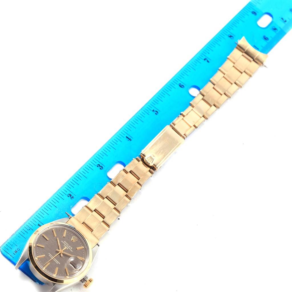 The image shows a top view of the Rolex Vintage Collection 1500 Men's Stainless Steel Brown Dial 1500 Men's Stainless Steel Brown Dial watch with its bracelet extended alongside a blue ruler.