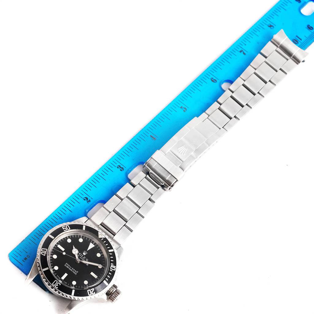 The image shows the full Rolex Vintage Collection 5513 Men
s Stainless Steel Black Dial 5513 Men
s Stainless Steel Black Dial watch laid flat next to a blue ruler, displaying the watch face and stainless steel bracelet.