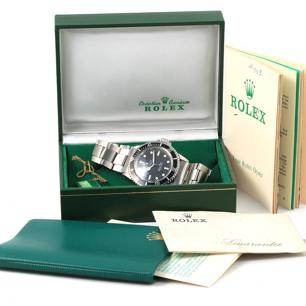 The Vintage Collection Rolex watch is shown in its open box with booklets, a guarantee card, and a green wallet.