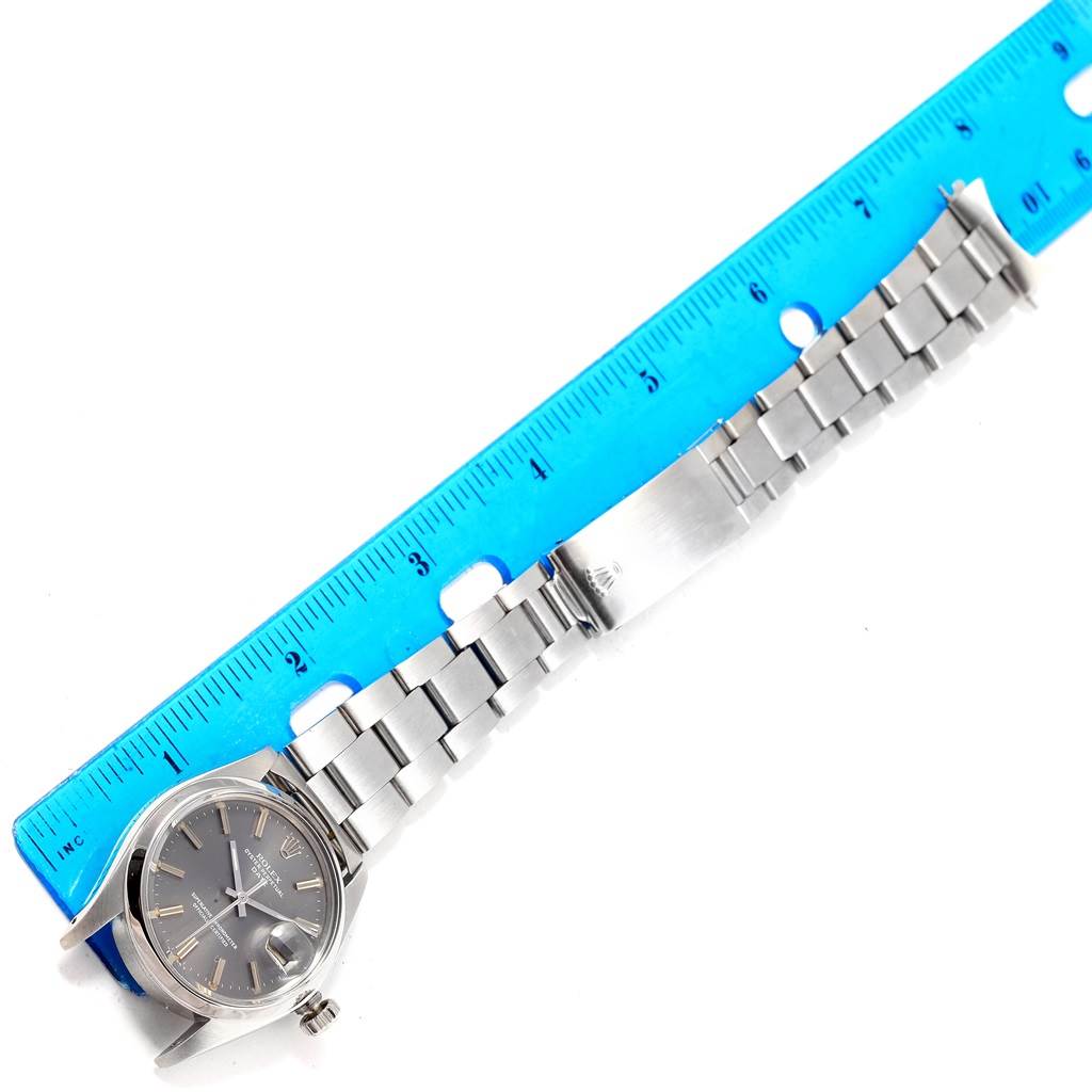 The Rolex Vintage Collection 1500 Men's Stainless Steel Grey Dial 1500 Men's Stainless Steel Grey Dial watch is laid flat beside a blue ruler, displaying its face, bracelet, and clasp.