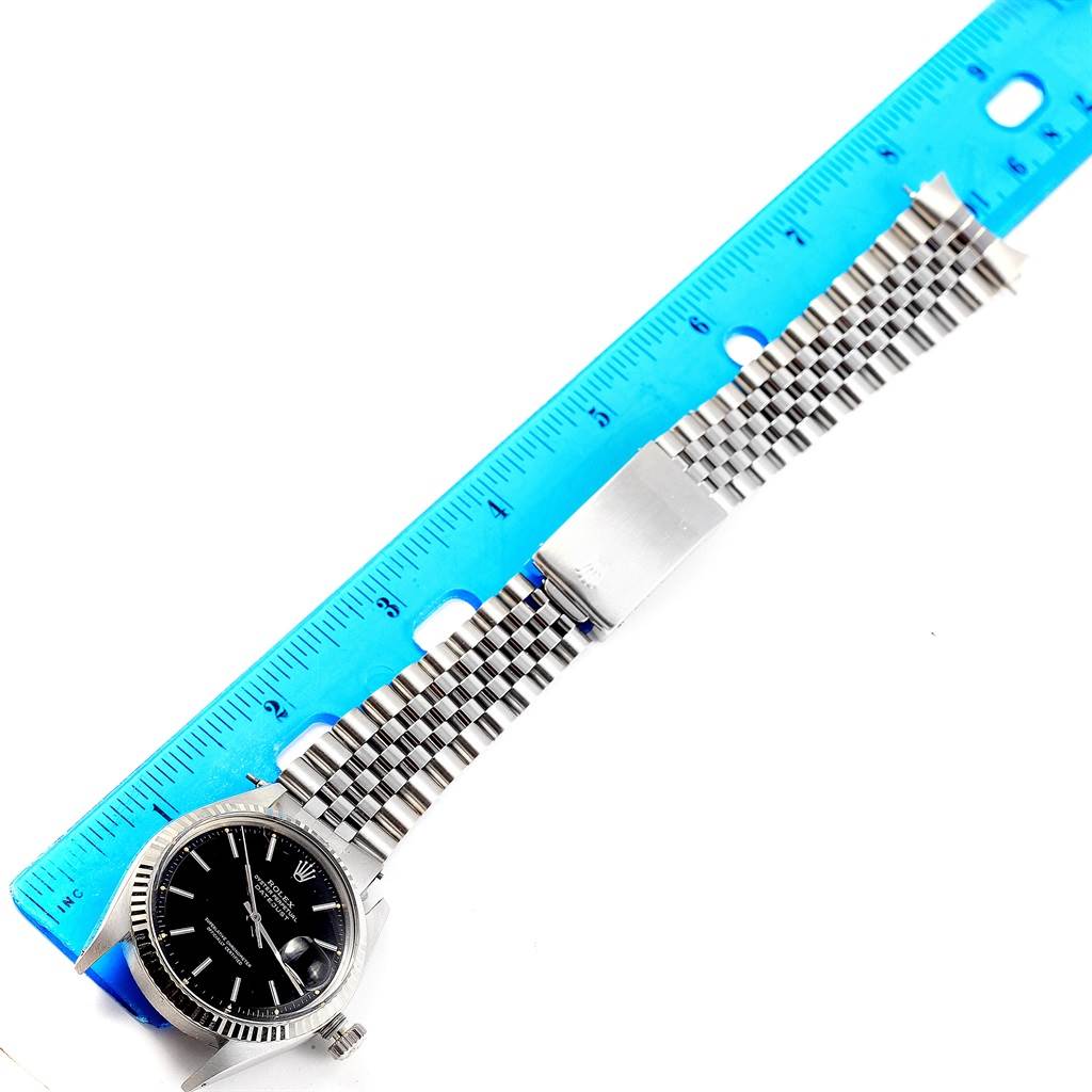 The Rolex Vintage Collection 1601 Men's Stainless Steel Black Dial 1601 Men's Stainless Steel Black Dial model watch is shown from a top-down angle with its face, bracelet, and a measuring ruler.