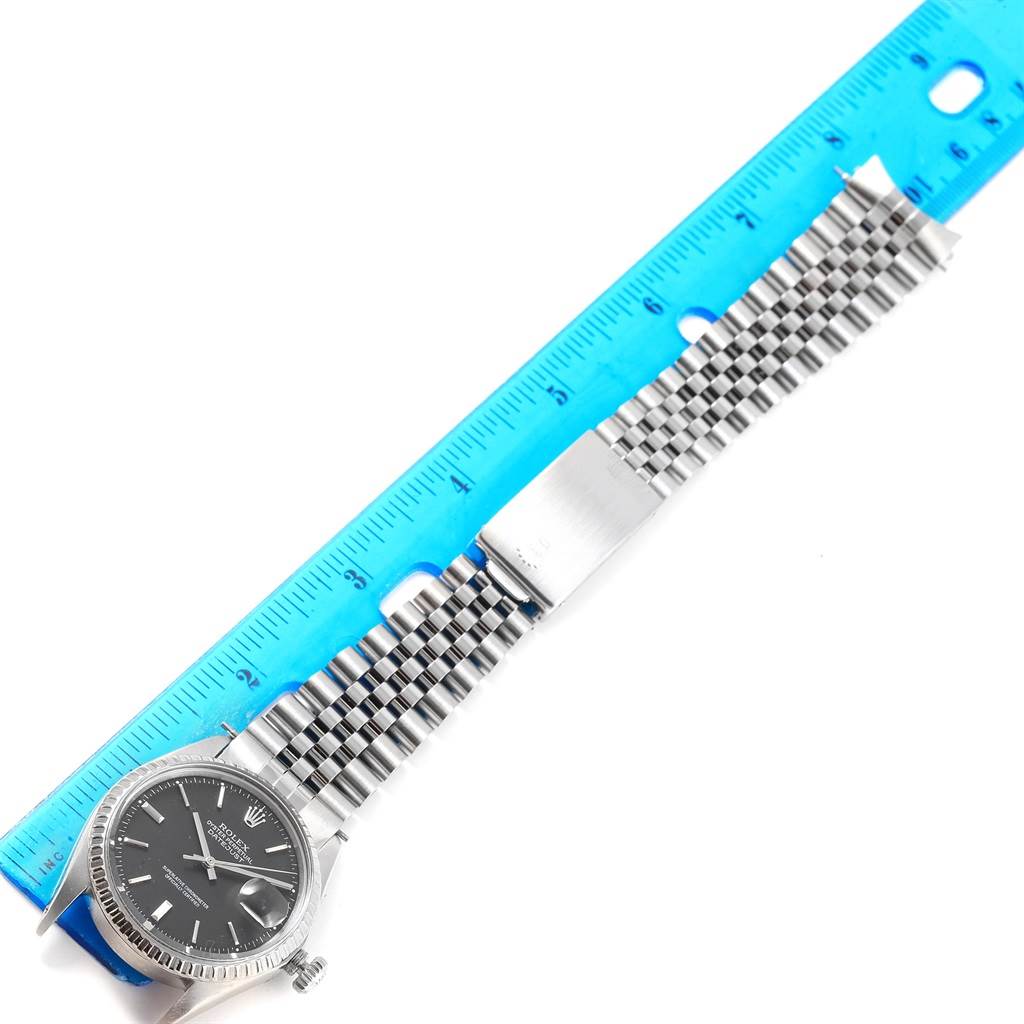 The image shows a Rolex Vintage Collection 1603 Men's Stainless Steel Black Dial 1603 Men's Stainless Steel Black Dial watch flat on a surface, with its metal bracelet next to a blue ruler.