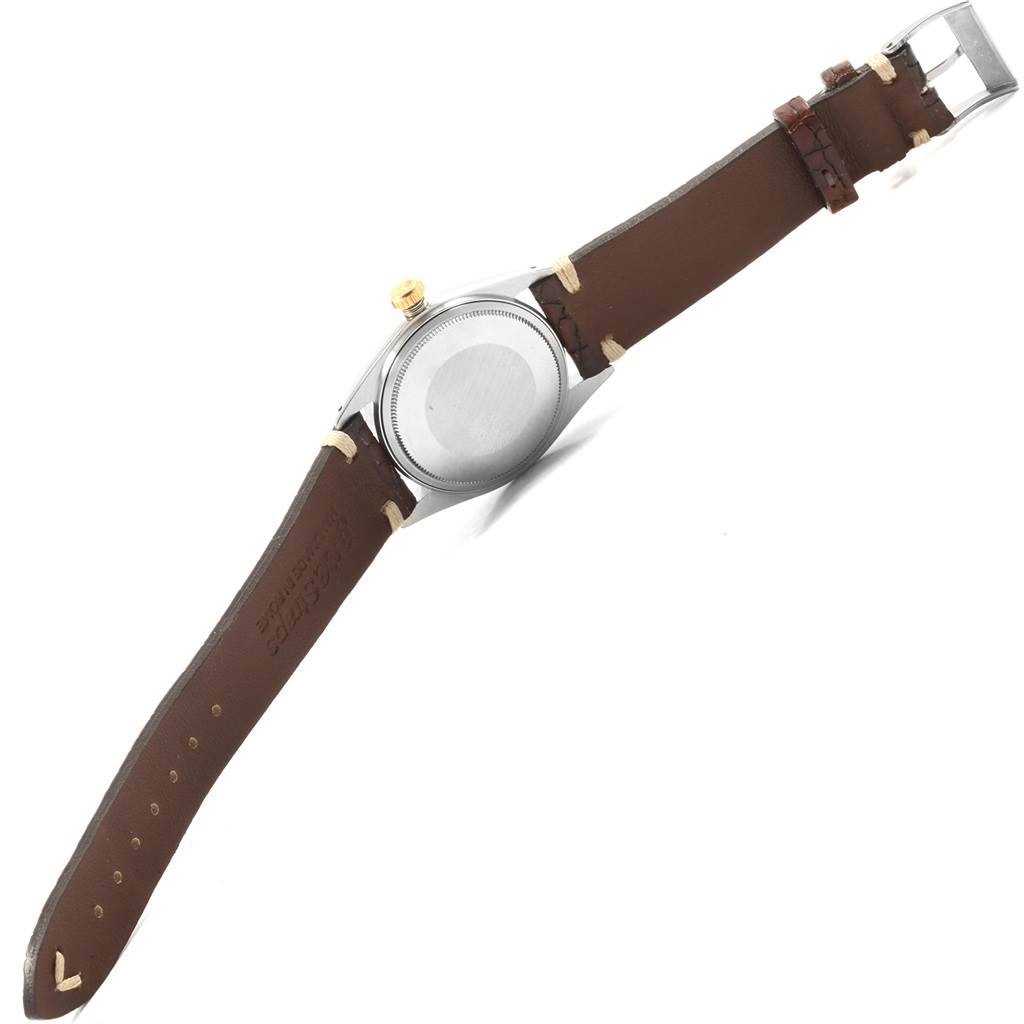 The image shows the back view of a Rolex Vintage Collection 1601 Men's Steel and Gold (two tone) Champagne Dial 1601 Men's Steel and Gold (two tone) Champagne Dial watch with a brown leather strap and a gold crown.