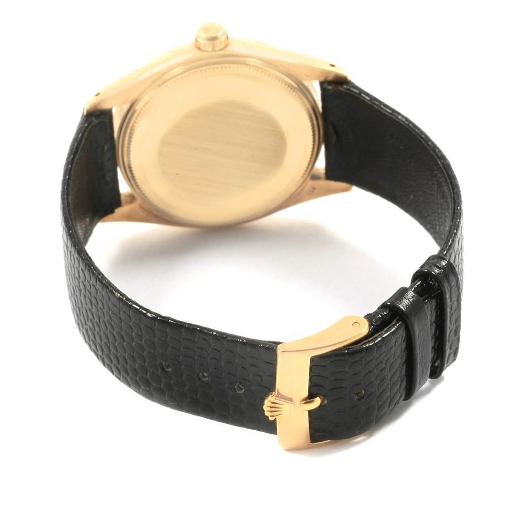 The image shows the back view of a Rolex Vintage Collection 1503 Men
s Yellow Gold Champagne Dial 1503 Men
s Yellow Gold Champagne Dial watch with a gold case and a black leather strap with a gold clasp.