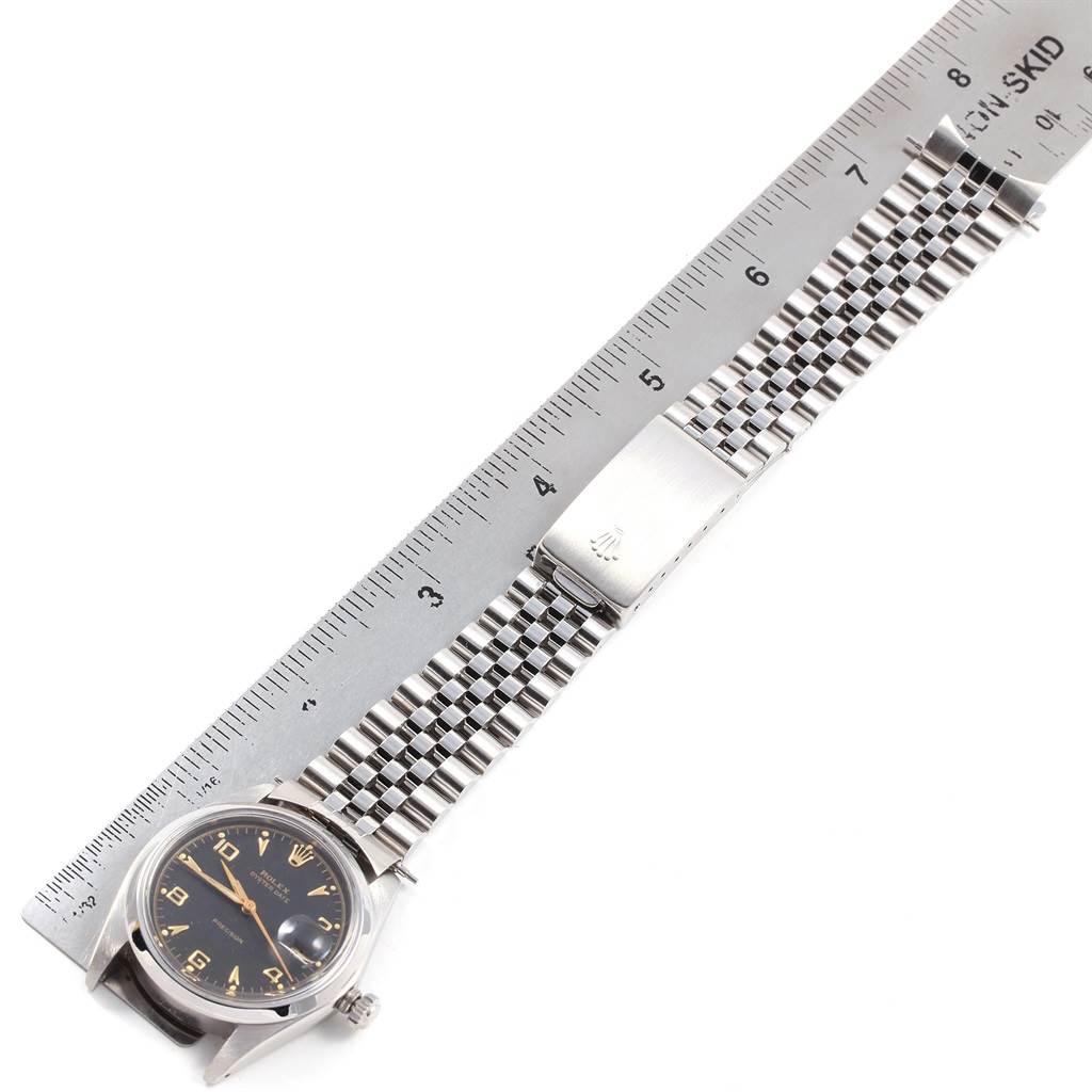 The image shows a top-down view of a Rolex Vintage Collection 6694 Men
s Stainless Steel Black Dial 6694 Men
s Stainless Steel Black Dial watch, focusing on the bracelet and the face beside a ruler.