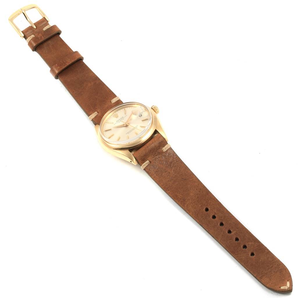 The image shows a Rolex Vintage Collection 1500 Men
s Yellow Gold Silver Dial 1500 Men
s Yellow Gold Silver Dial watch from a top-down angle, featuring a beige dial, gold case, and brown leather strap.