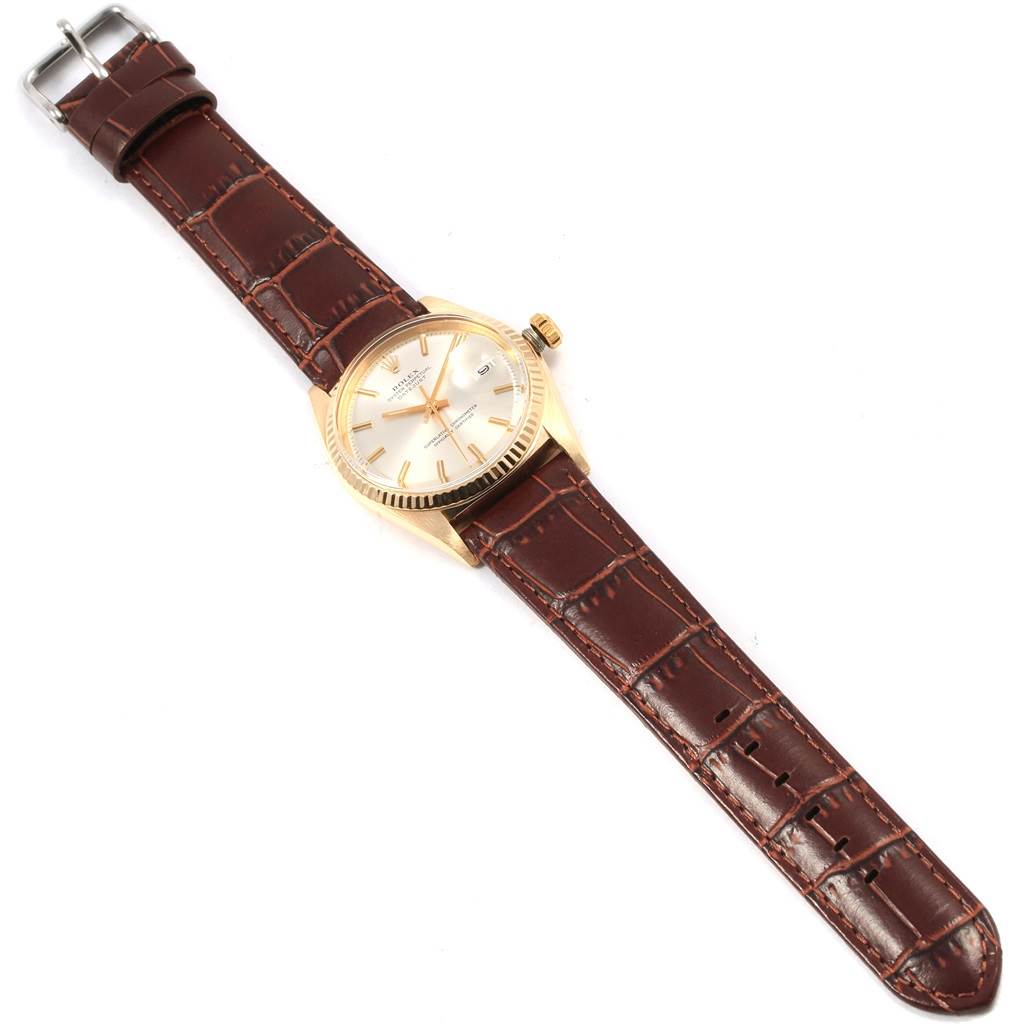This Rolex Vintage Collection 1601 Men
s Yellow Gold Silver Dial 1601 Men
s Yellow Gold Silver Dial watch is shown from a top-down angle, highlighting its brown leather strap, gold casing, and face.