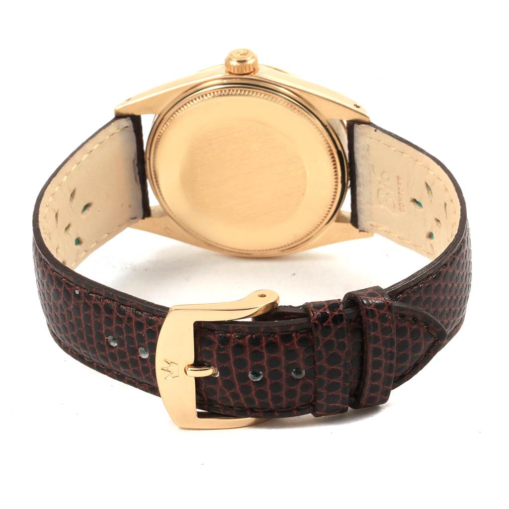 The image shows the back of the Rolex Vintage Collection 1503 Men's Yellow Gold Silver Dial 1503 Men's Yellow Gold Silver Dial watch with a gold case and a brown leather strap with a gold buckle.