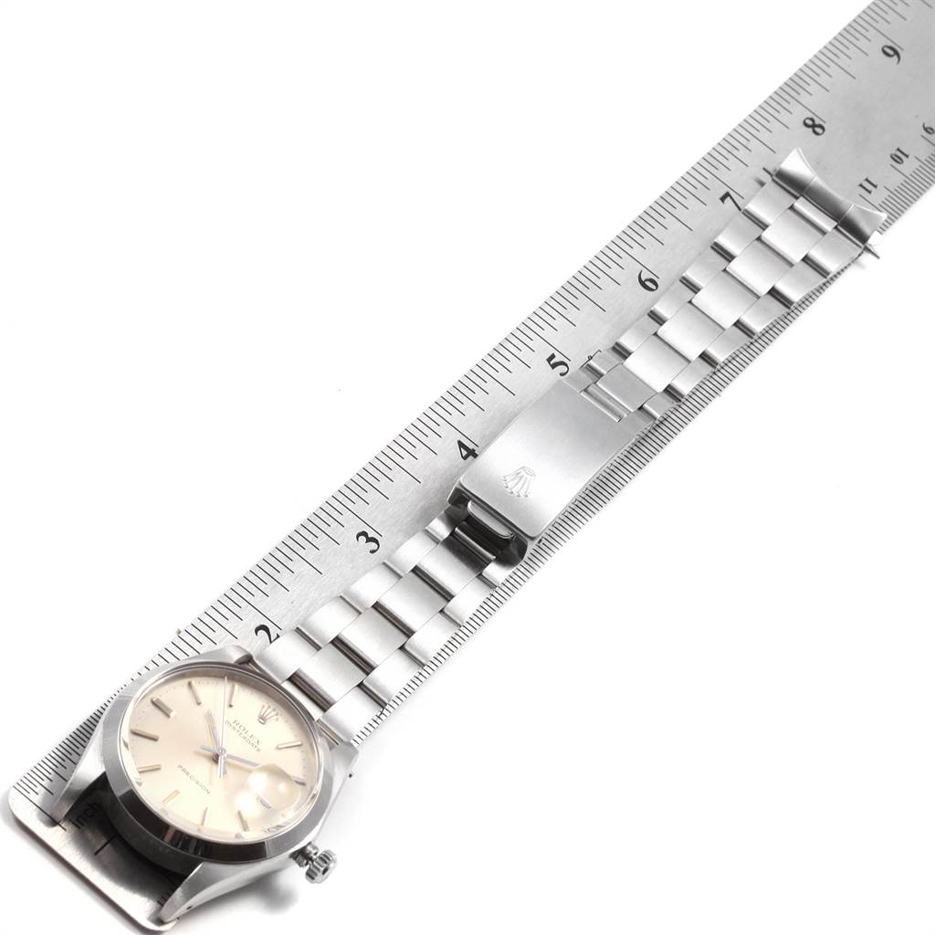 The image shows a top-view angle of a Rolex Vintage Collection 6694 Men
s Stainless Steel Silver Dial 6694 Men
s Stainless Steel Silver Dial watch laid on a ruler, displaying the face and metal bracelet.