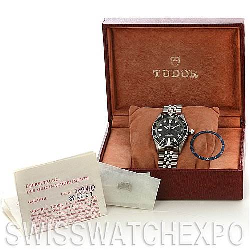 The Tudor Submariner 90910 Men's Stainless Steel Black Dial 90910 Men's Stainless Steel Black Dial watch is displayed at a front angle with its bezel removed and warranty documents included in the box.