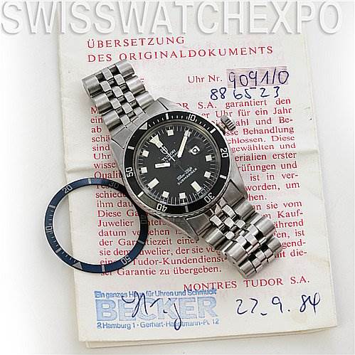 The Tudor Submariner 90910 Men's Stainless Steel Black Dial 90910 Men's Stainless Steel Black Dial watch is displayed face-up with a metal bracelet, alongside a replacement bezel insert and documentation.