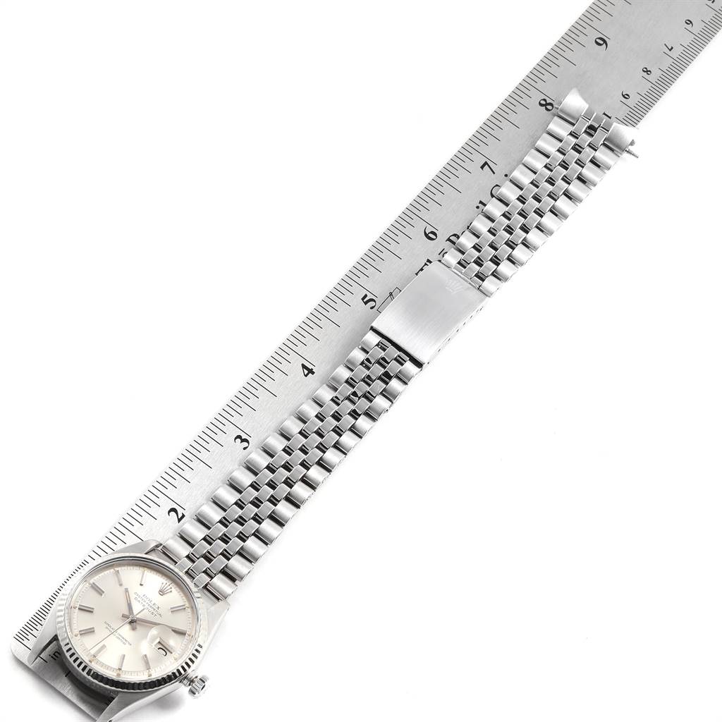 The image shows an overhead view of a Rolex Vintage Collection 1601 Men's Stainless Steel Silver Dial 1601 Men's Stainless Steel Silver Dial watch and its metal bracelet next to a ruler.