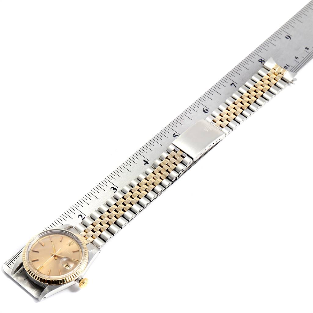 The image shows the front of a Rolex Vintage Collection 1601 Men's Steel and Gold (two tone) Brown Dial 1601 Men's Steel and Gold (two tone) Brown Dial watch placed diagonally on a ruler, displaying its face and two-tone bracelet.