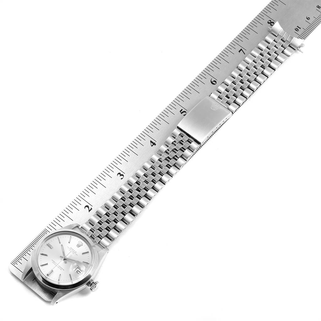 This image shows a Rolex Vintage Collection 1500 Men
s Stainless Steel Silver Dial 1500 Men
s Stainless Steel Silver Dial watch with its face and metal bracelet laid alongside a ruler.