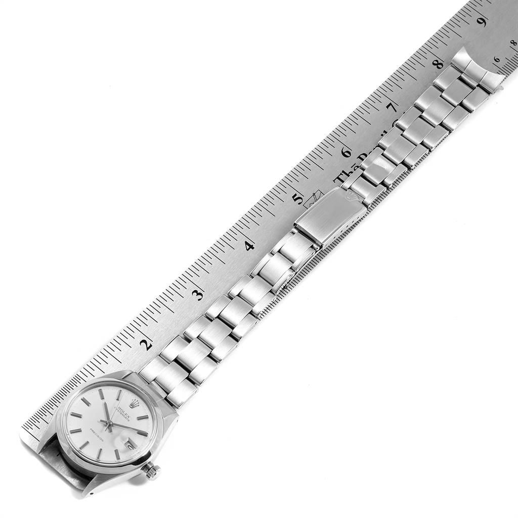 The image shows a Rolex Vintage Collection 6694 Men
s Stainless Steel Silver Dial 6694 Men
s Stainless Steel Silver Dial watch laid flat next to a ruler, displaying its face, bracelet, and clasp.