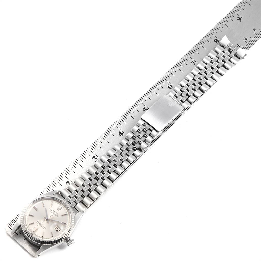 The image shows a Rolex Vintage Collection 1601 Men
s Stainless Steel Silver Dial 1601 Men
s Stainless Steel Silver Dial watch laid flat on a ruler, displaying its face, bracelet, and clasp.