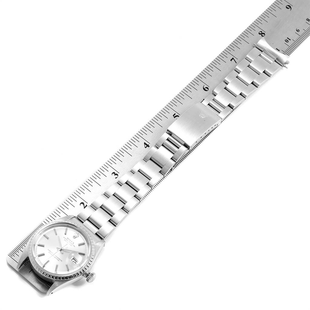 The Rolex Vintage Collection 1603 Men
s Stainless Steel Silver Dial 1603 Men
s Stainless Steel Silver Dial watch is shown at an angled top view, highlighting its face, bracelet, and clasp beside a ruler.