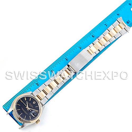 The image shows a top view of a Rolex Vintage Collection 1500 Men's Steel and Gold (two tone) Black Dial 1500 Men's Steel and Gold (two tone) Black Dial watch placed next to a blue ruler, highlighting its band and face.