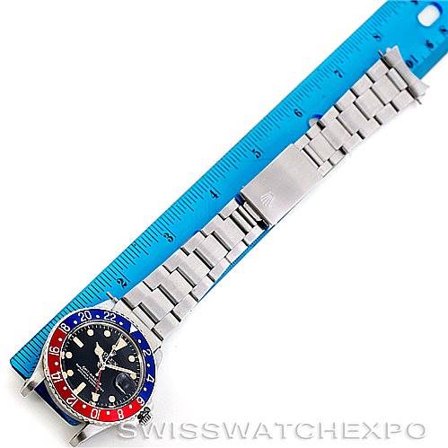 The image shows a top-down view of the Rolex Vintage Collection 1675 Men's Stainless Steel Black Dial 1675 Men's Stainless Steel Black Dial watch placed next to a blue ruler for size reference.