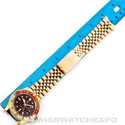 The image shows a Rolex Vintage Collection 1675 Men's Yellow Gold Brown Dial 1675 Men's Yellow Gold Brown Dial model watch laid flat next to a blue ruler, displaying its face and full linked bracelet.