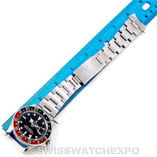 The image shows a top-down view of a Rolex Vintage Collection 1675 Men's Stainless Steel Black Dial 1675 Men's Stainless Steel Black Dial watch beside a blue ruler, focusing on the watch's face and metal bracelet.