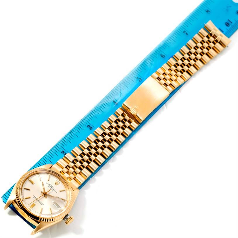 The Rolex Vintage Collection 1601 Men's Yellow Gold Silver Dial 1601 Men's Yellow Gold Silver Dial watch is shown from a top-down angle, displaying the face, case, and entire bracelet next to a blue ruler.